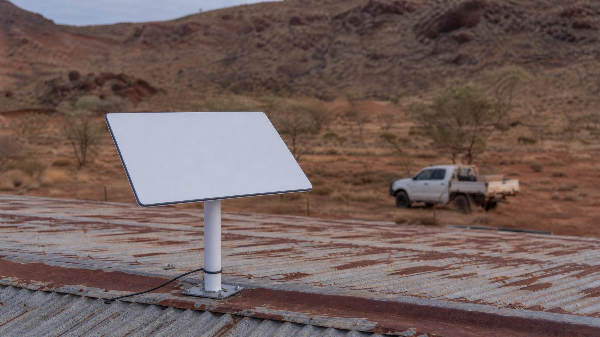 Starlink dish mounted on a tin shed roof at a remote Western Australian pastoral station, with rust-red Pilbara dirt and spinifex in the foreground