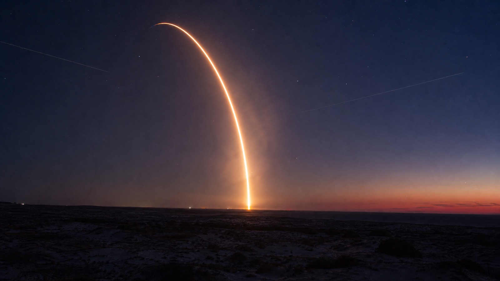 Long-exposure photo of a Falcon 9 launch arc against a twilight sky
