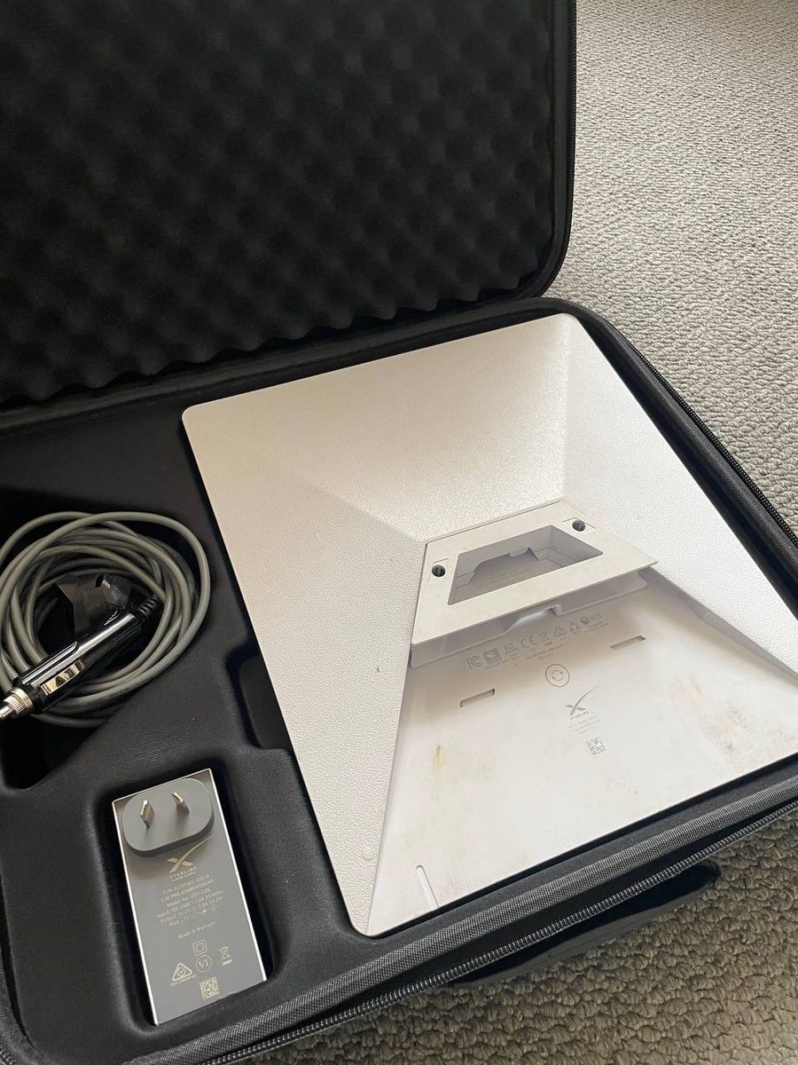 The underside of a Starlink Mini showing the fold-out kickstand and the mounting slot, with the vehicle power lead beside it